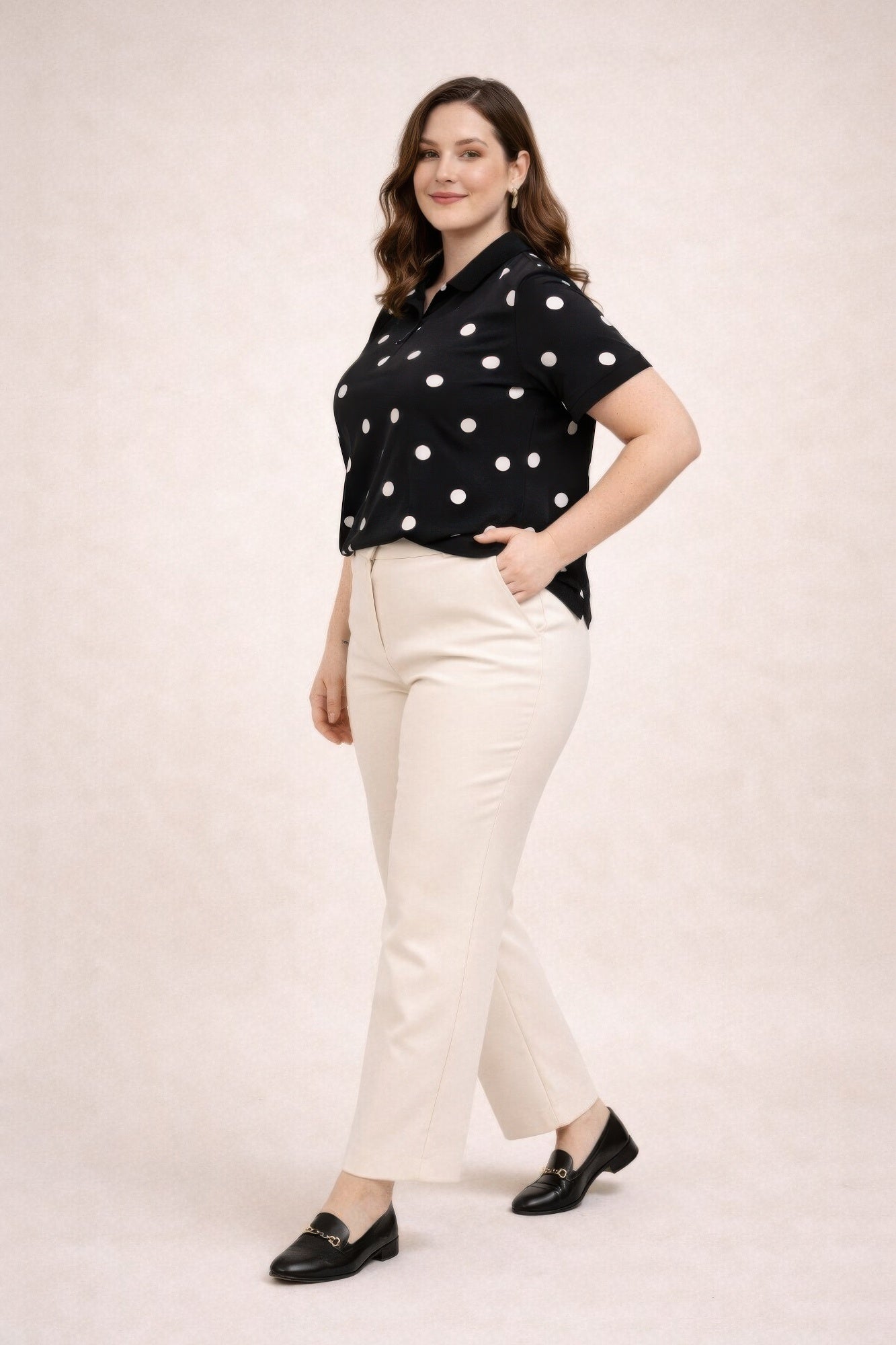 Woman wearing a black polka dot shirt and white pants on a plain background
