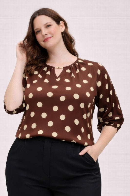 Woman wearing a brown blouse with white polka dots on a plain background