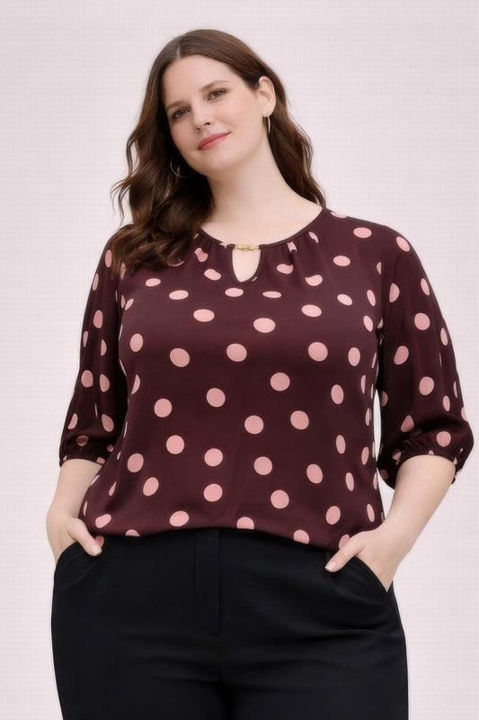 Woman wearing a maroon blouse with pink polka dots against a light background
