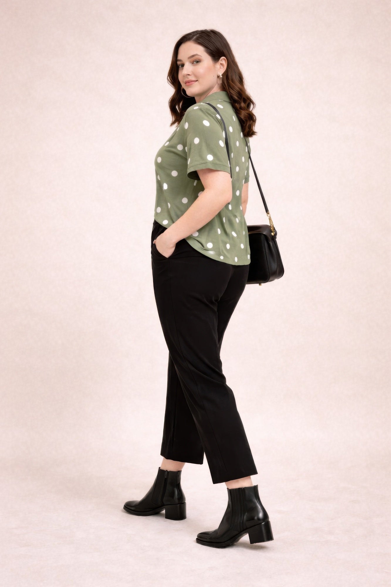 Woman wearing a green polka dot blouse, black pants, and black boots on a beige background