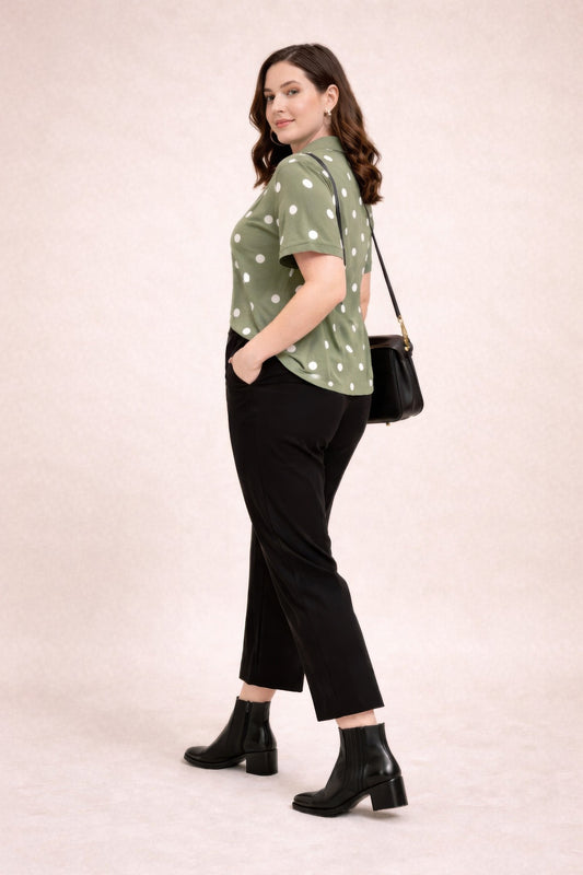 Woman wearing a green polka dot blouse, black pants, and black boots on a beige background