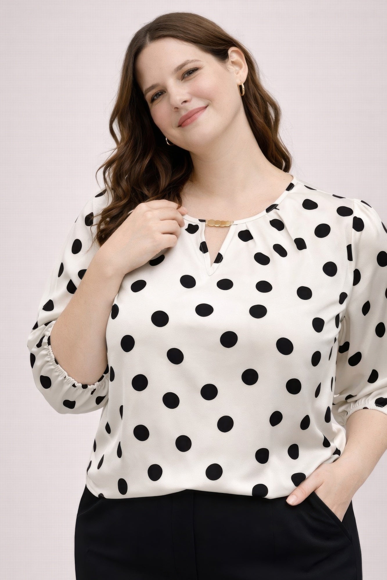 Woman wearing a white blouse with black polka dots against a plain background
